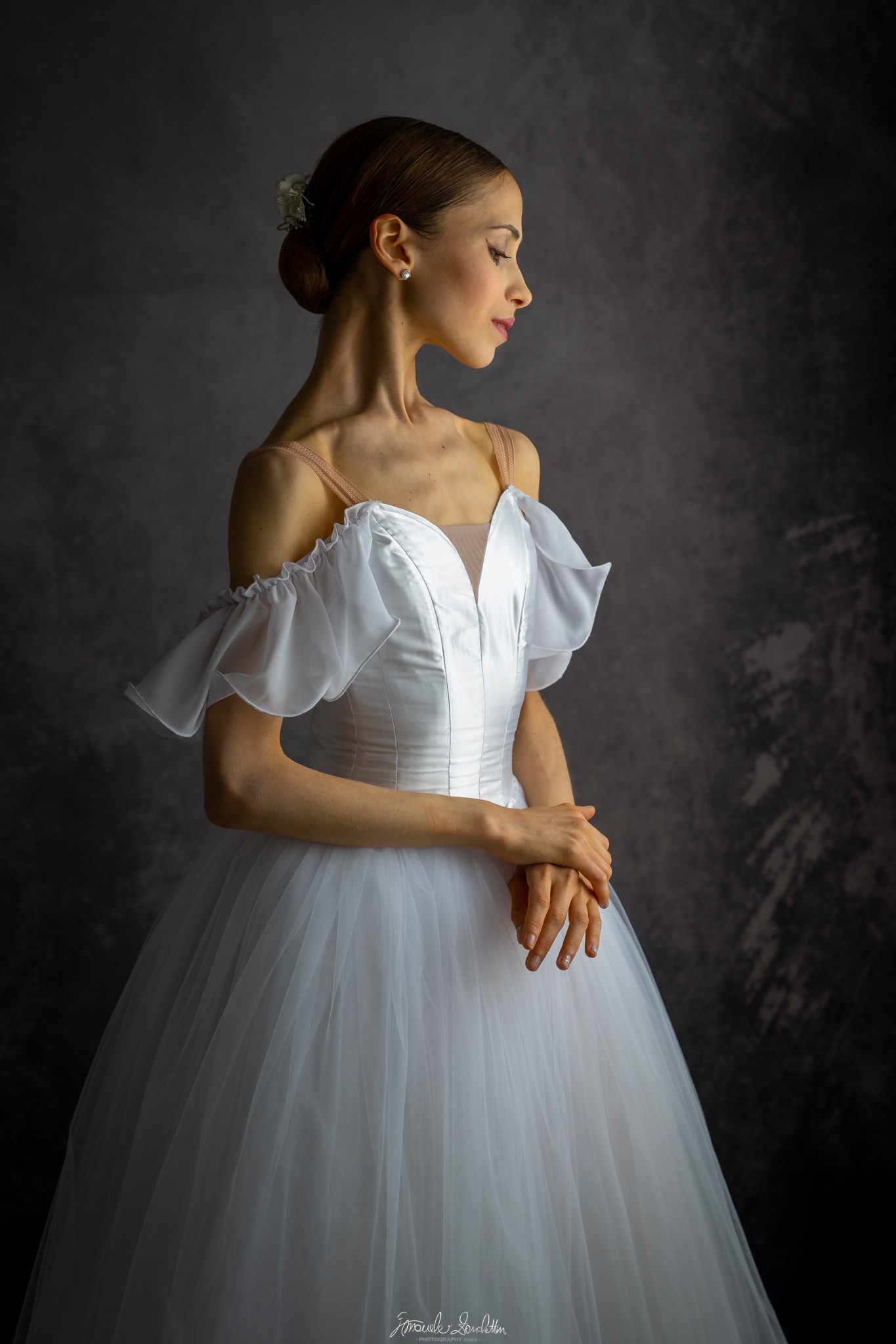 A poised ballerina in a white dress against a dark studio backdrop