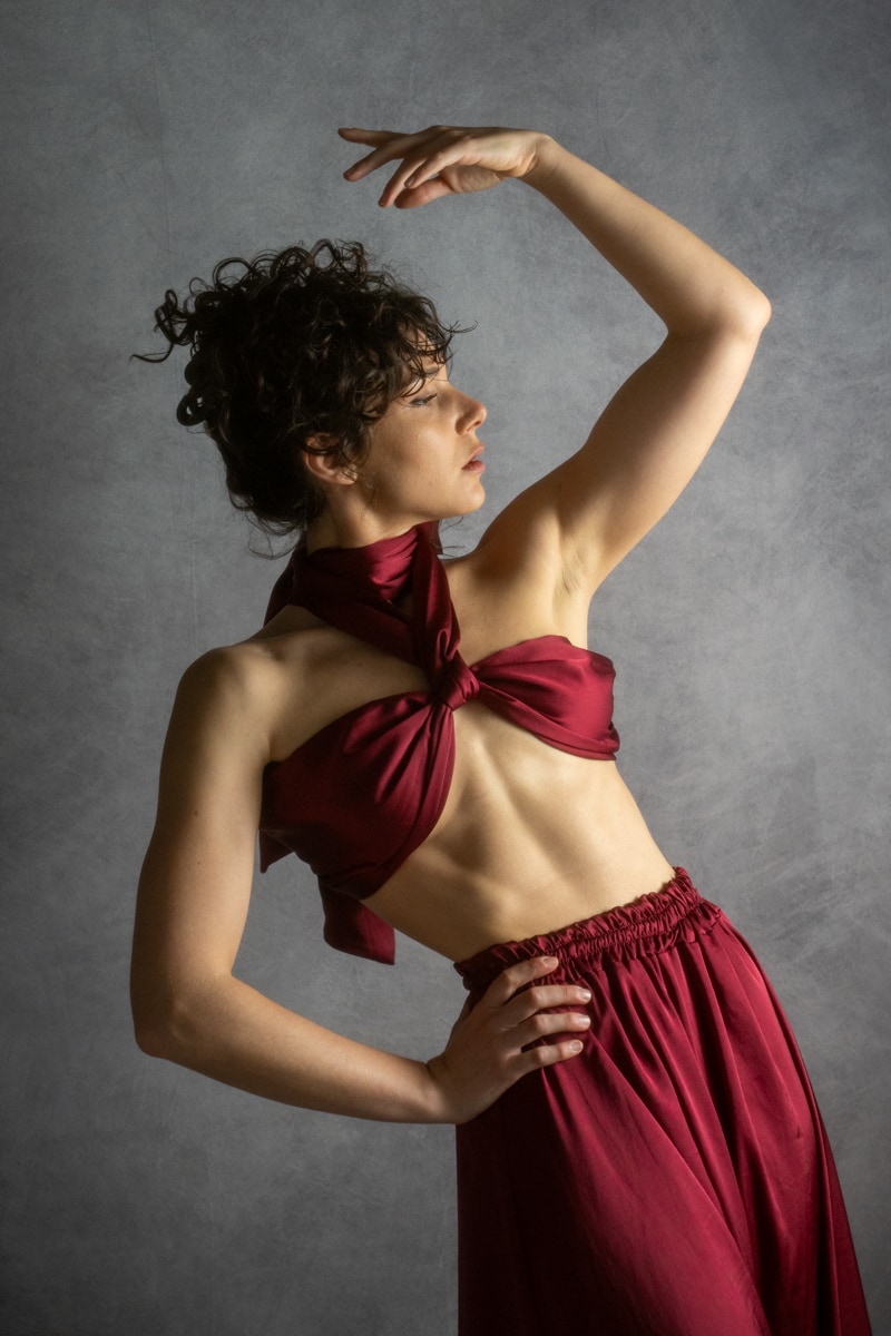 A dancer in burgundy forming a curved pose against a grey backdrop