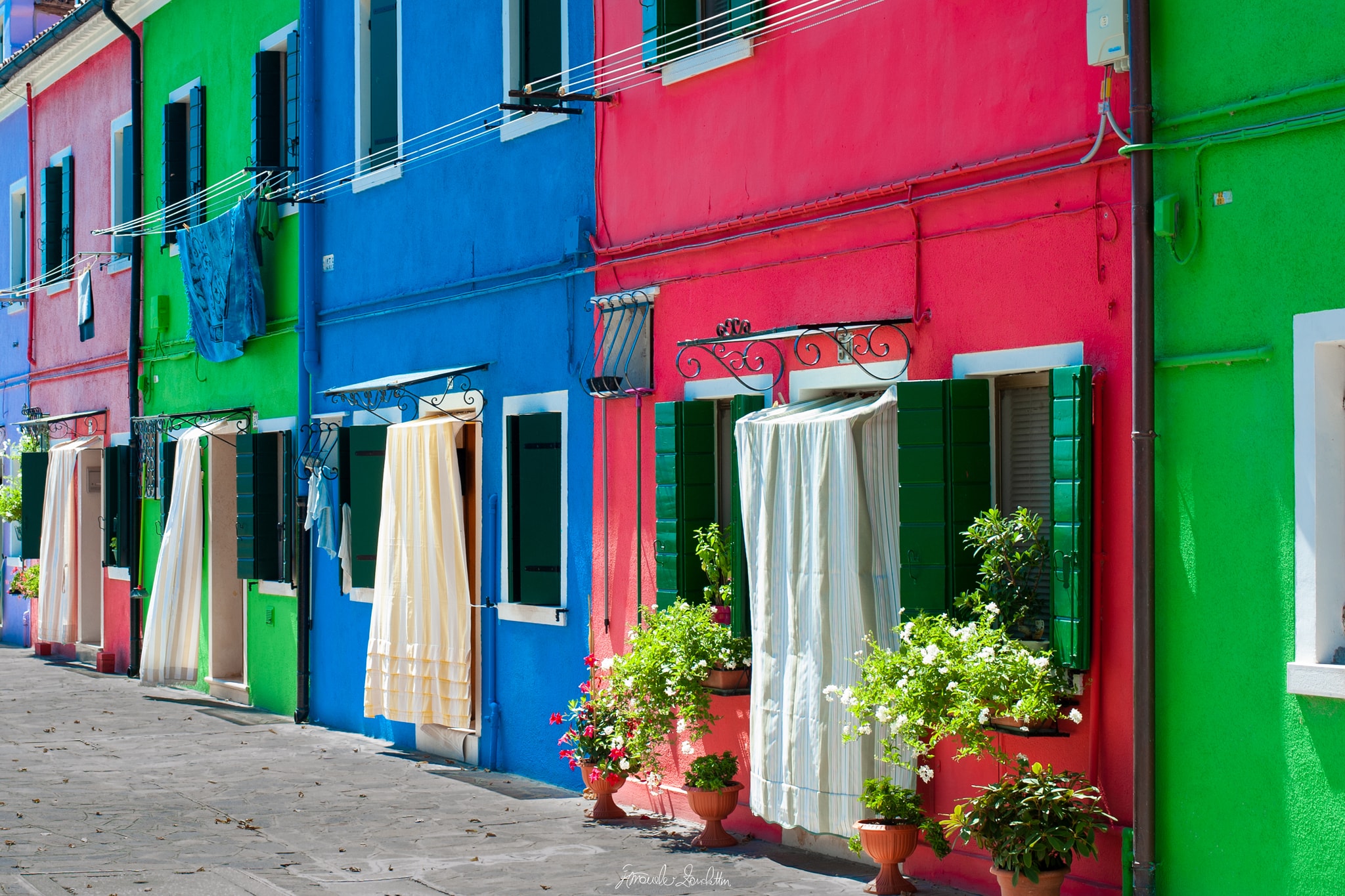 Bright green, blue and pink homes on Burano with dark shutters, washing lines, sheets and potted plants