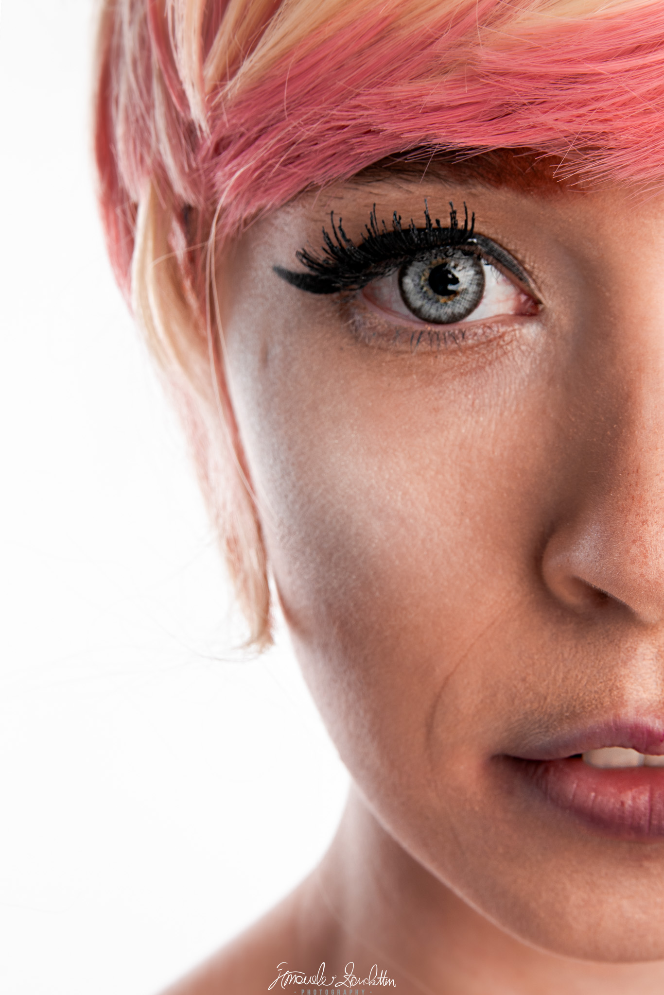 Ritratto ravvicinato e luminoso di una donna con capelli rosa, trucco grafico e un occhio grigio, con metà volto inquadrato