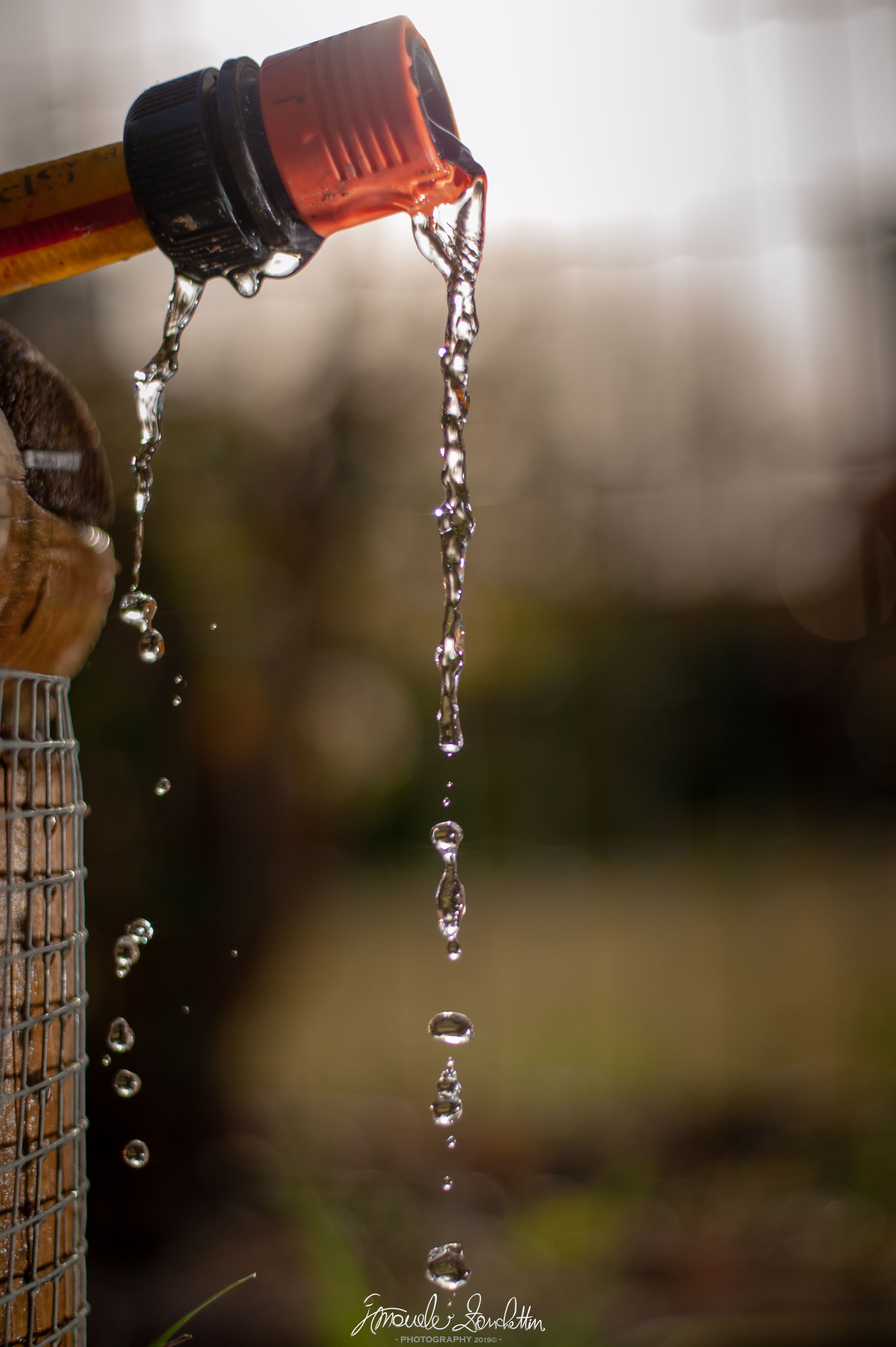 Acqua che scorre dalle setole di un pennello con manico arancione e si spezza in gocce sospese