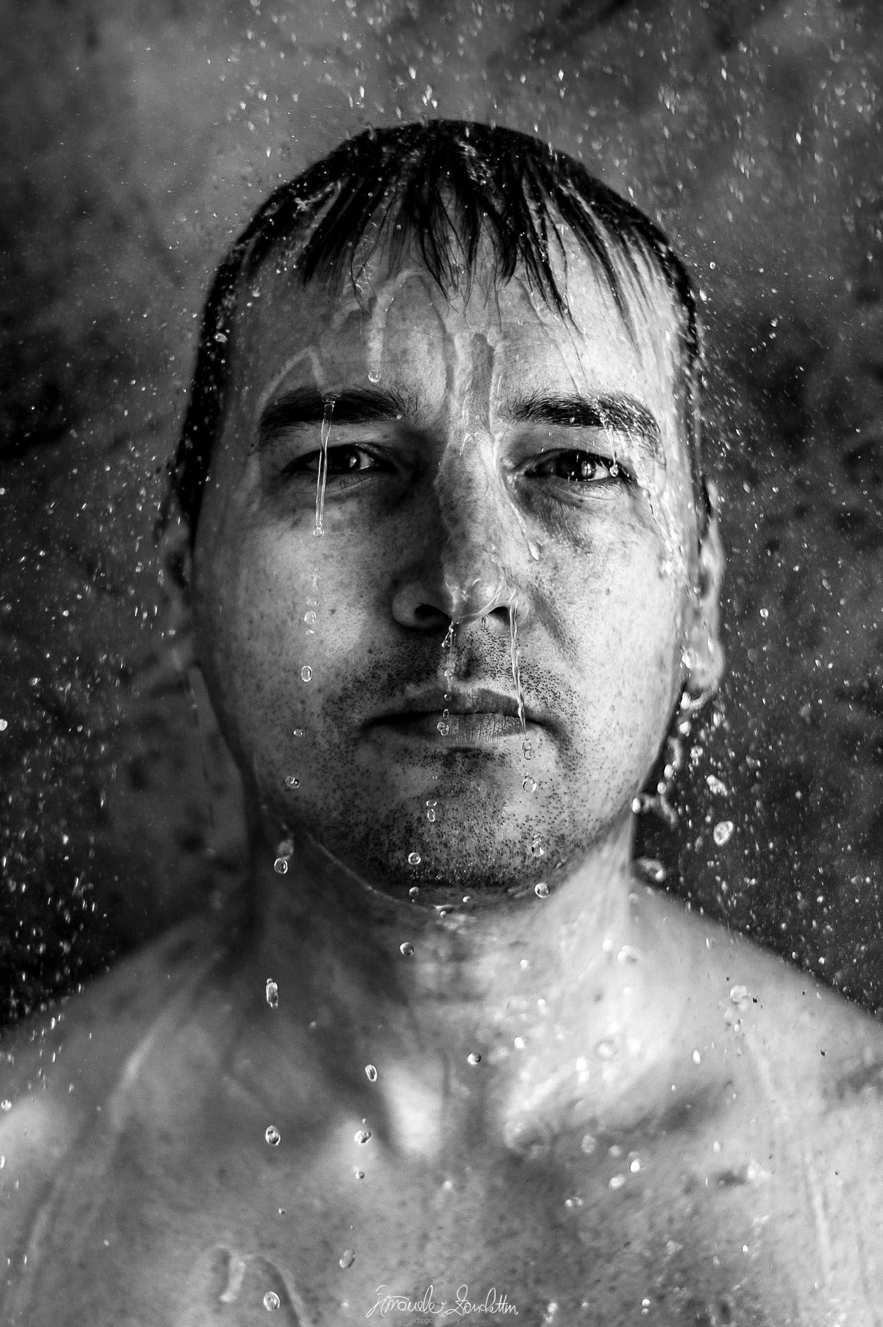 Ritratto ravvicinato in bianco e nero di un uomo circondato da gocce e fili d’acqua sospesi