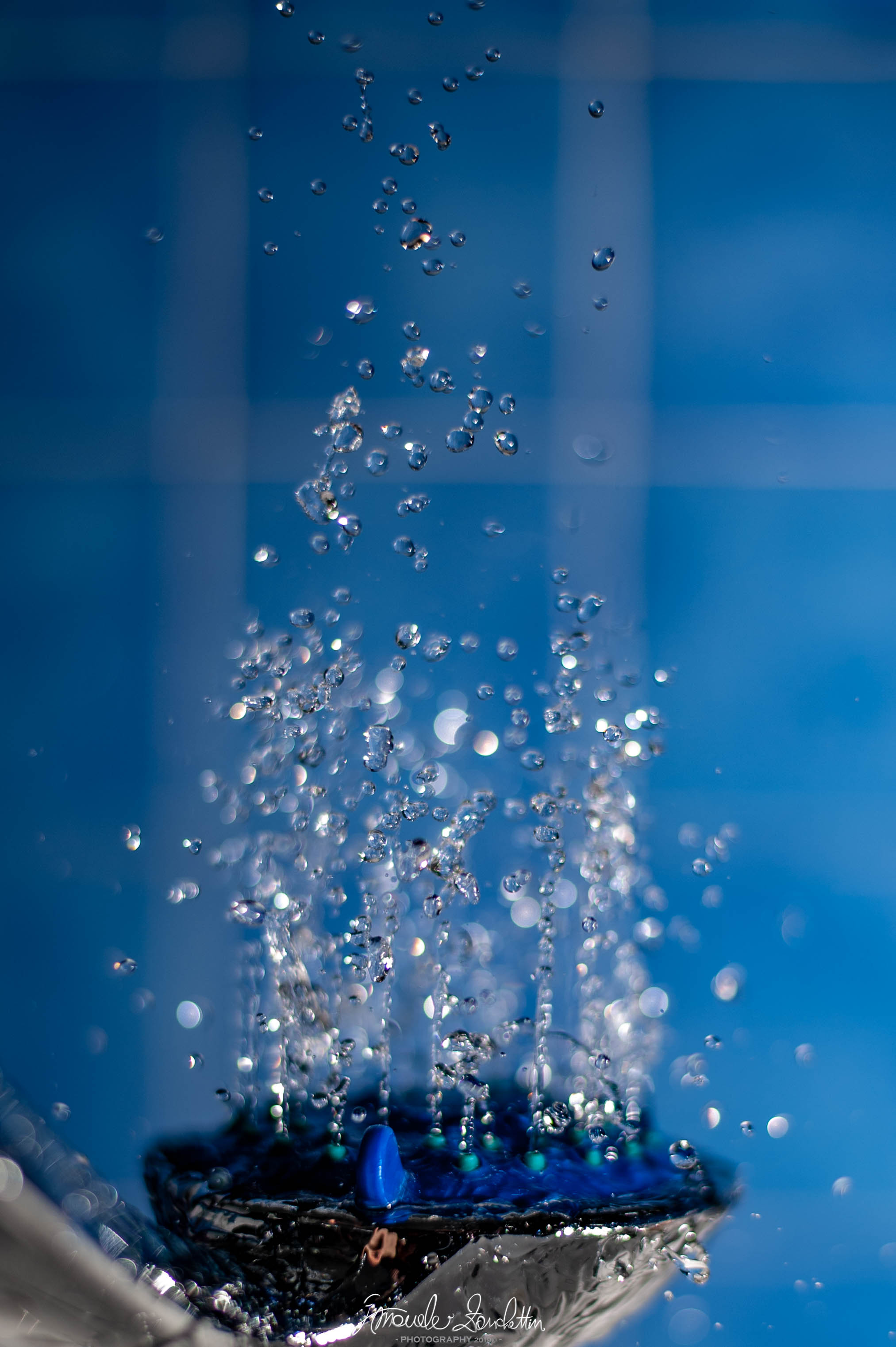 Una colonna d’acqua che si spezza in molte gocce sospese contro uno sfondo blu