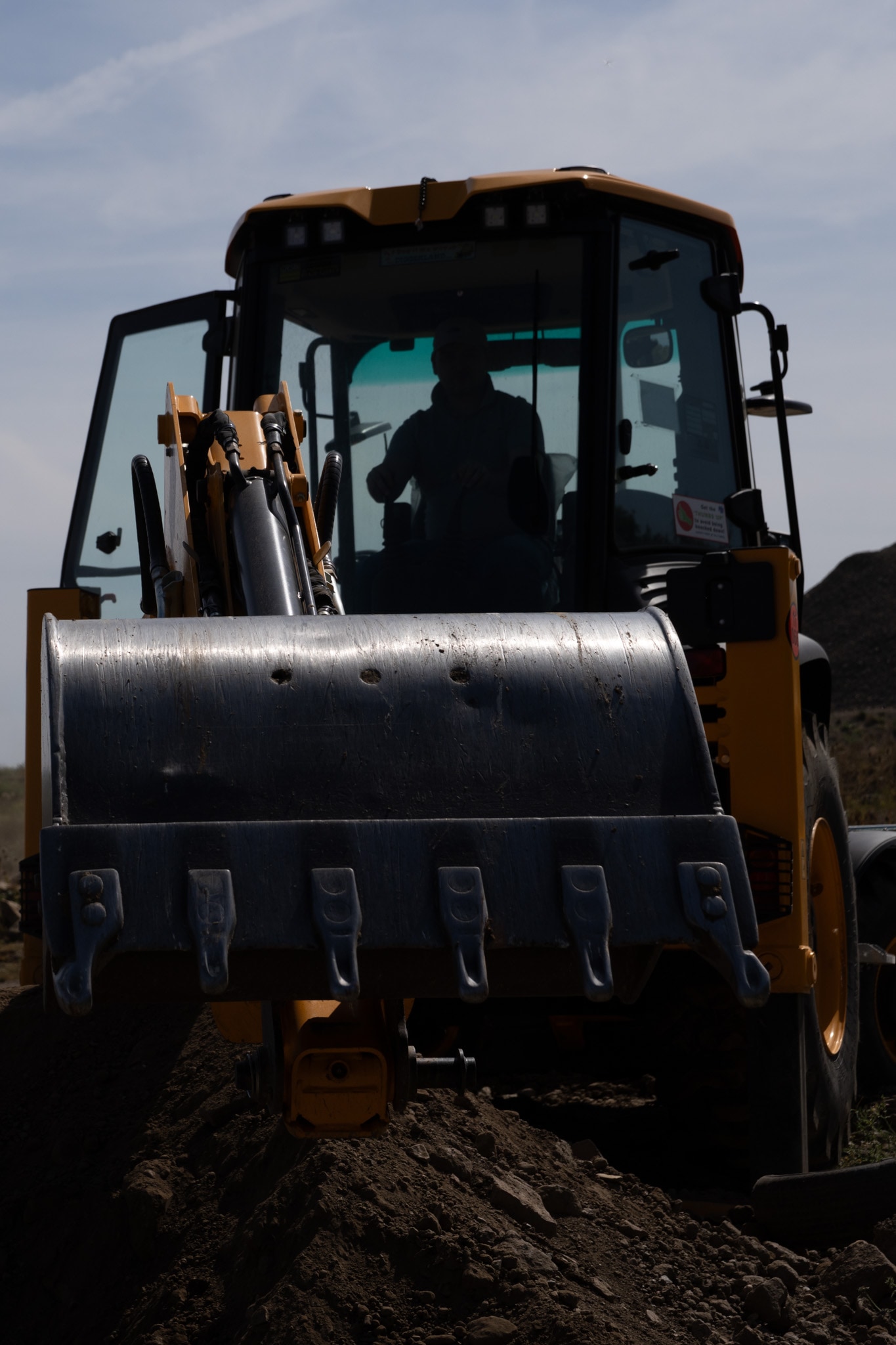 Before editing: a front loader photographed against a bright sky, with the cab, bucket and ground very dark