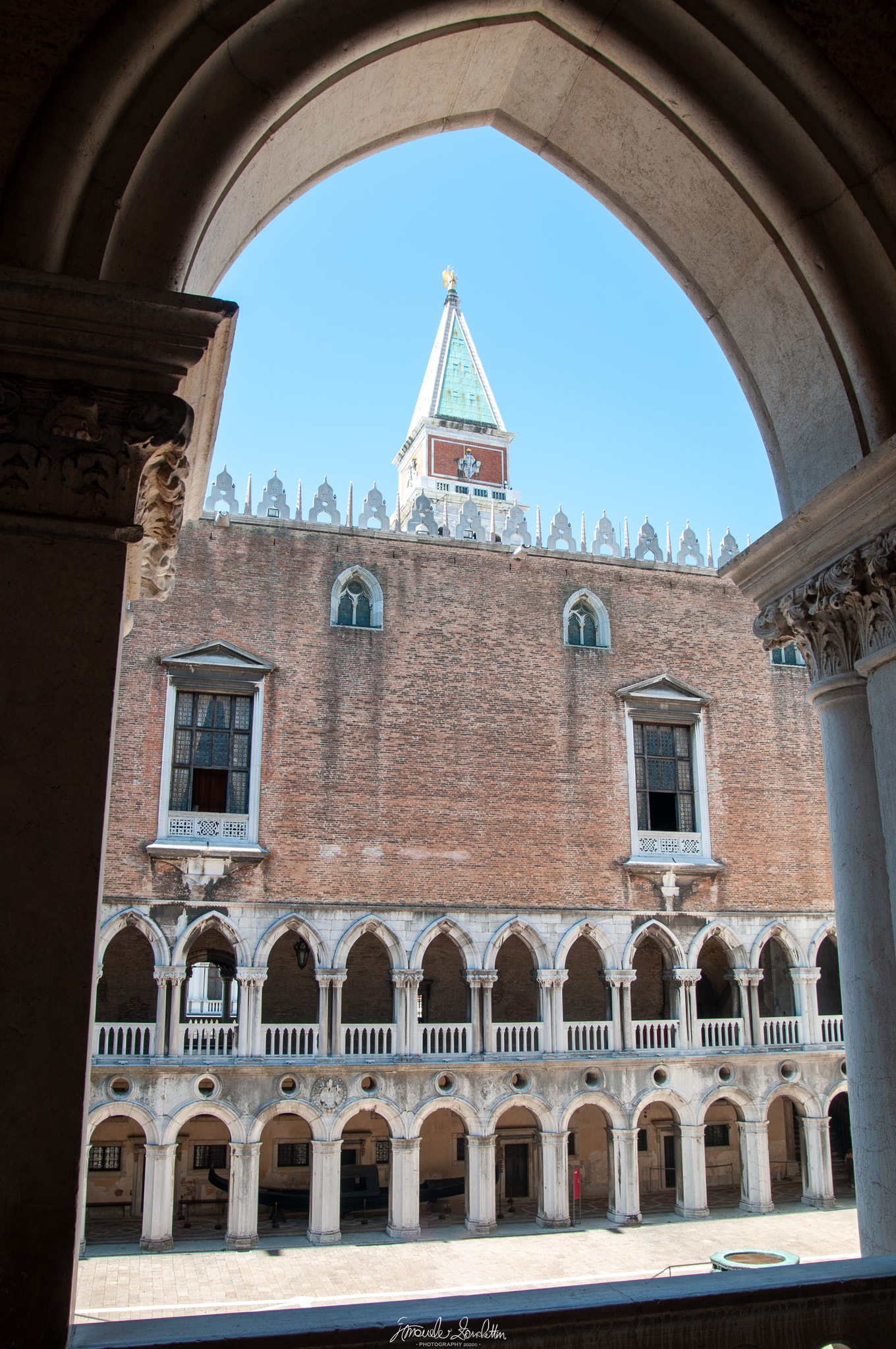 Venetian palace façade and bell tower framed through the deep shadow of a large stone arch