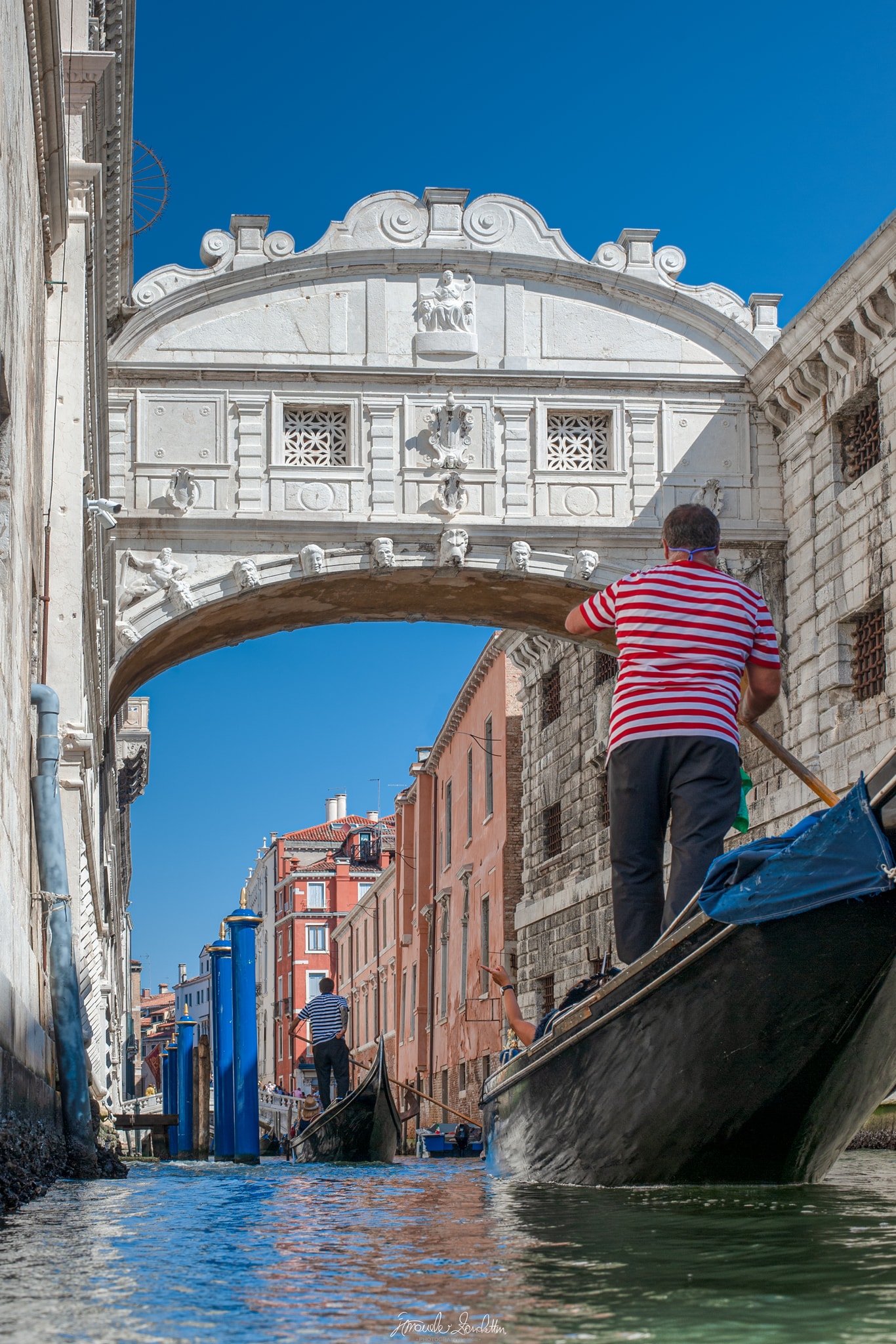 Low view from a Venetian canal with a gondolier in the foreground and the Bridge of Sighs spanning the scene above